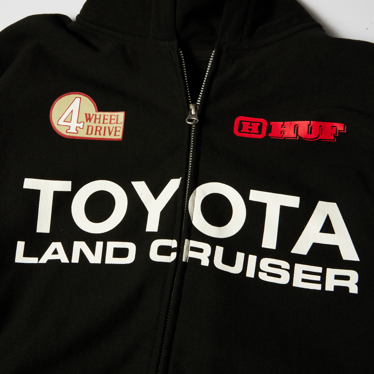 Hoodie à fermeture éclair HUF x Toyota Land Cruiser Heavyweight noir — détail de la fermeture et des logos sur la poitrine.